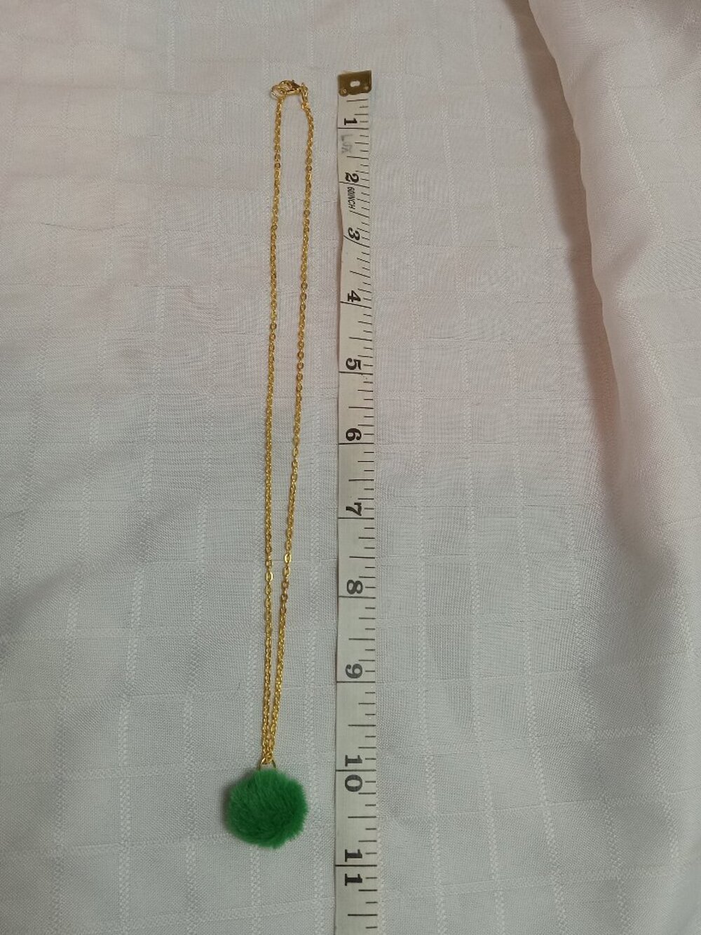 Handmade necklace with a small pom-pom and gold-colored accent hooks and chains